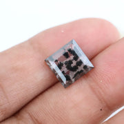 Clear lab-grown diamond with striking black natural-style inclusions inside a polished rectangular crystal, showcasing a unique modern gemstone aesthetic