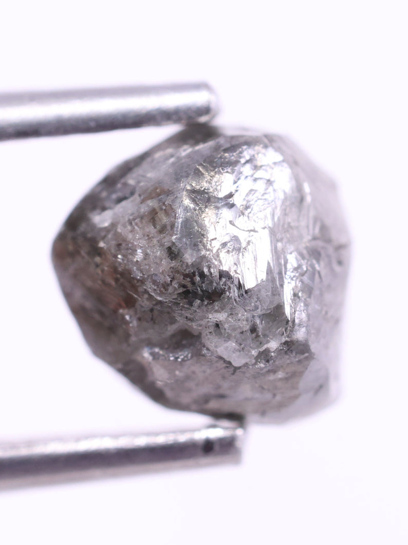 Raw diamond held between tweezers on a white background