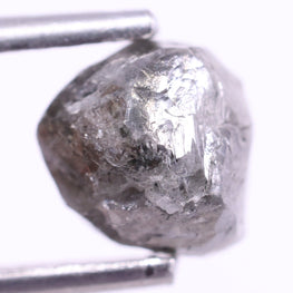 Raw diamond held between tweezers on a white background