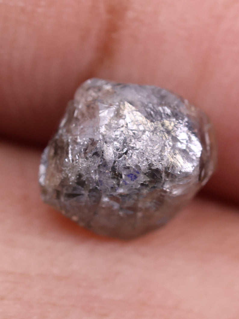 Raw diamond held between fingers against a neutral background