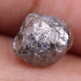Raw diamond held between fingers against a neutral background