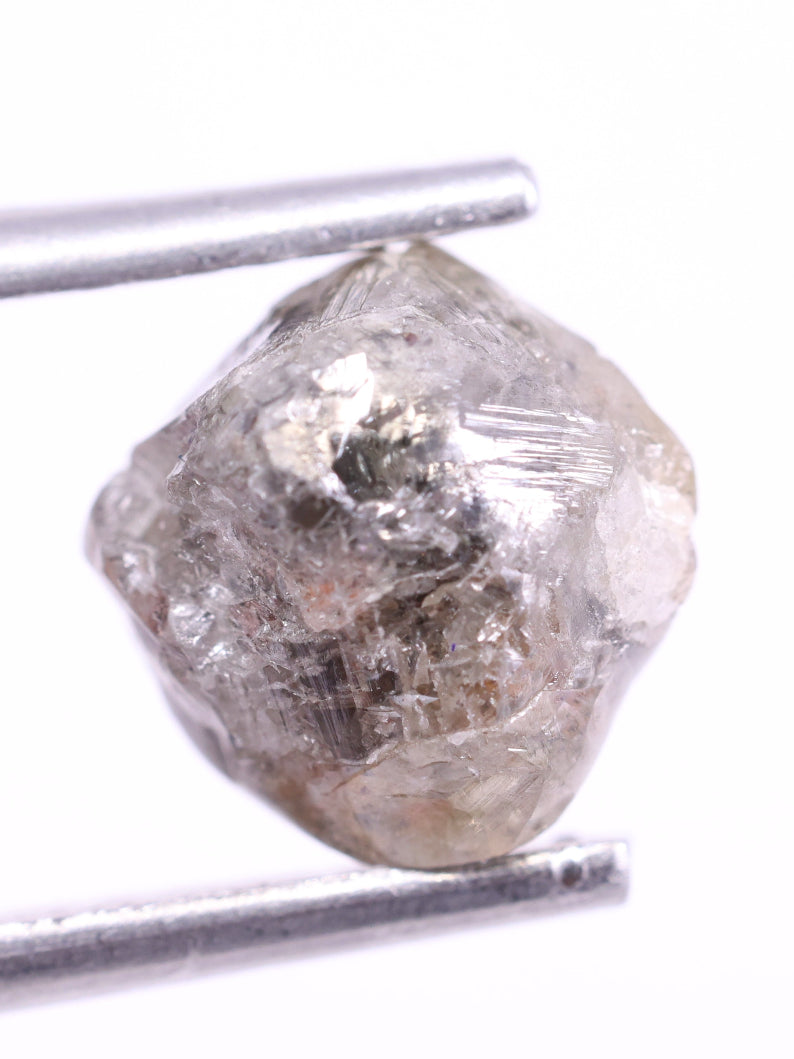 Raw diamond held between tweezers on a white background