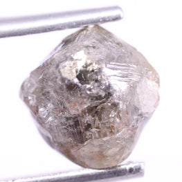 Raw diamond held between tweezers on a white background