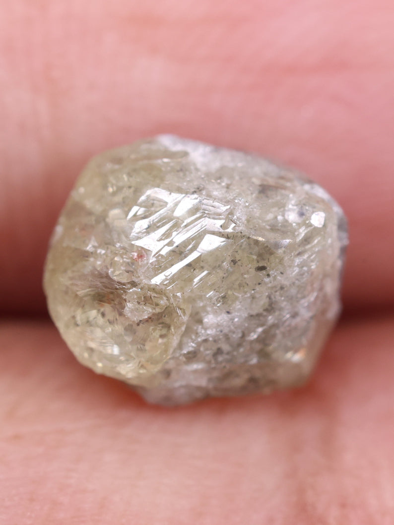 Raw diamond held between fingers against a blurred background