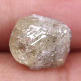 Raw diamond held between fingers against a blurred background