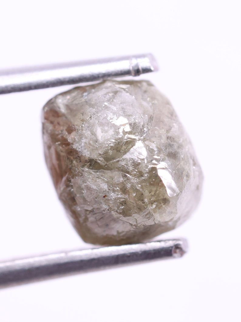 Raw diamond held between tweezers on a white background