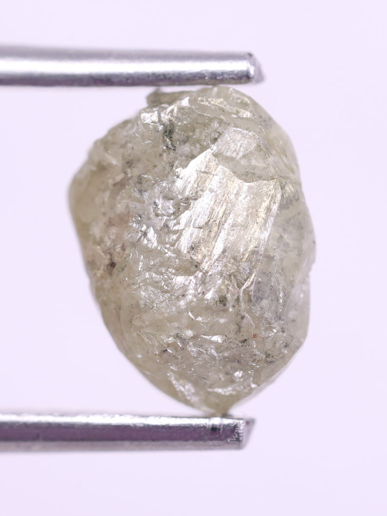 Raw diamond held between tweezers on a light purple background