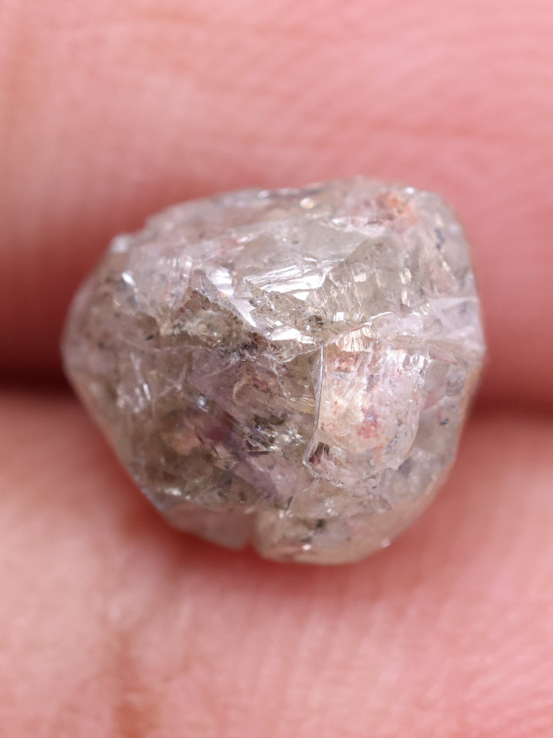Raw diamond held by tweezers on a white background