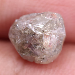 Raw diamond held by tweezers on a white background