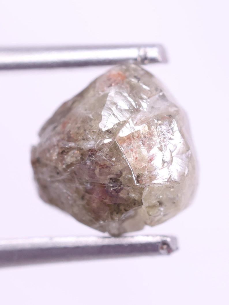 Raw diamond held by tweezers on a white background
