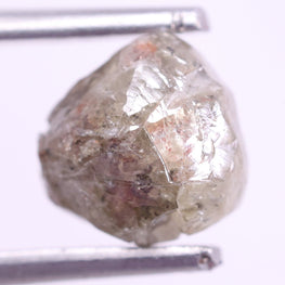 Raw diamond held by tweezers on a white background