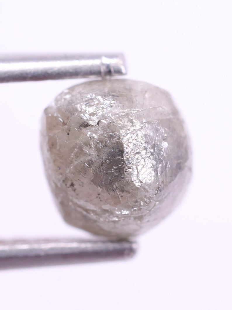 Raw diamond held between tweezers on a white background