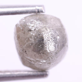 Raw diamond held between tweezers on a white background