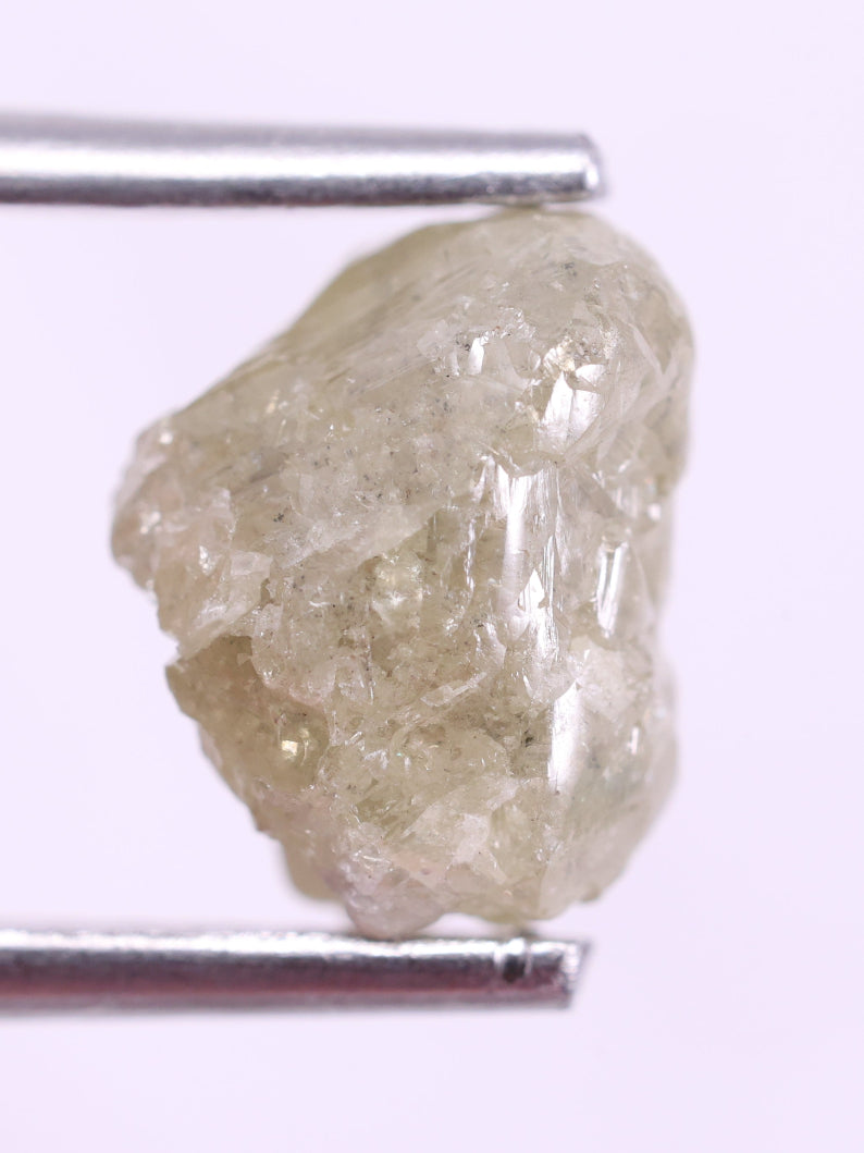 Raw diamond held by tweezers on a white background