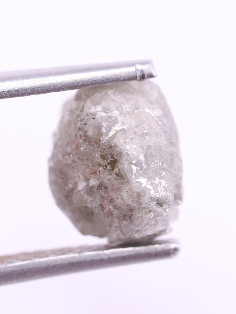 Raw diamond held by tweezers on a white background