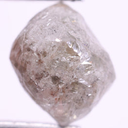 Raw diamond held by tweezers on a white background