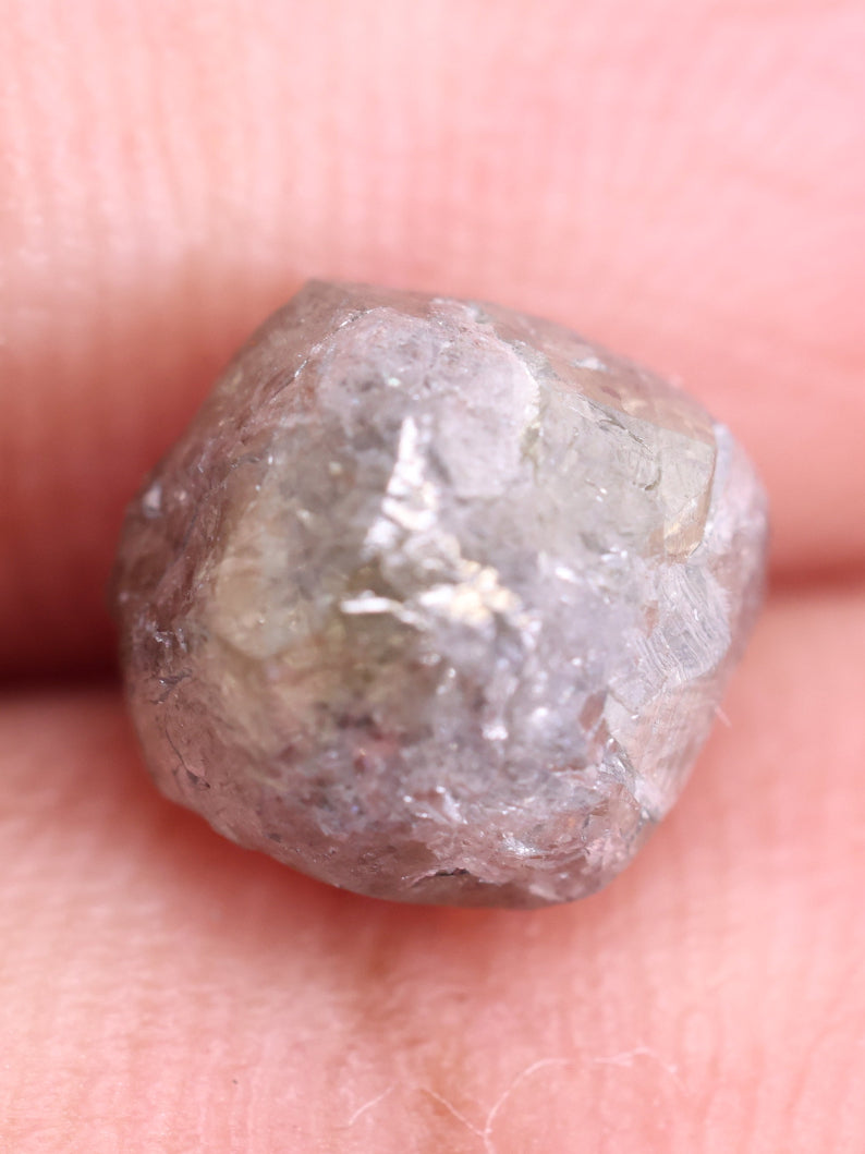 Raw diamond held between fingers on a light pink background