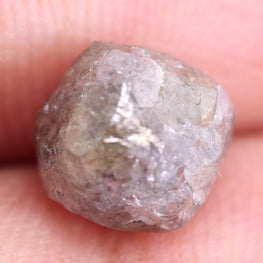 Raw diamond held between fingers on a light pink background