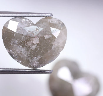 Heart-shaped diamond held by tweezers on a light background