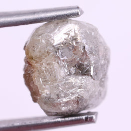 Raw diamond held by tweezers on a light purple background