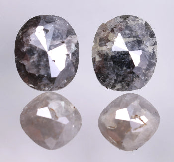 Two oval-cushion shaped diamonds on a reflective surface with a light gray background