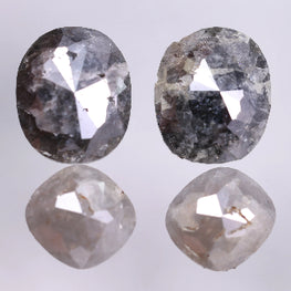 Two oval-cushion shaped diamonds on a reflective surface with a light gray background
