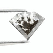 Geometric cut salt and pepper lab grown diamond with smoky black and white inclusions, showcasing a unique faceted shape and modern ethical gemstone design on a clean white background