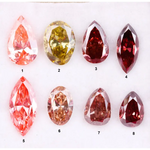 Eight faceted lab grown colored diamonds in pear, oval, and marquise cuts featuring fancy pink, yellow, and deep red tones arranged on a white background.