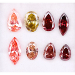 Eight faceted lab grown colored diamonds in pear, oval, and marquise cuts featuring fancy pink, yellow, and deep red tones arranged on a white background.