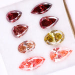 Eight faceted lab grown colored diamonds in pear, oval, and marquise cuts featuring fancy pink, yellow, and deep red tones arranged on a white background.