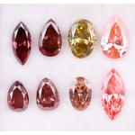 Eight faceted lab grown colored diamonds in pear, oval, and marquise cuts featuring fancy pink, yellow, and deep red tones arranged on a white background.