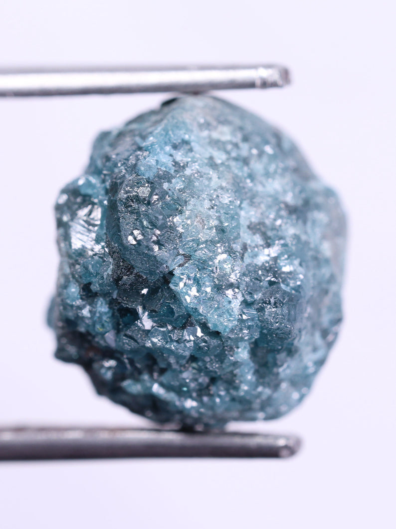Raw blue diamond held by tweezers on a white background