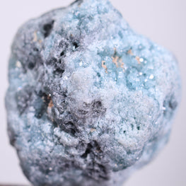Blue natural diamond rock held by tweezers on a light gray background