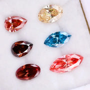 Six fancy color lab grown diamonds on white background including yellow oval cut, blue marquise cut, pink marquise cut, peach pear cut, deep red pear cut, and red oval cut brilliant stones for custom jewelry design.