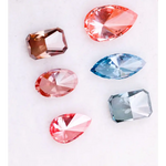 Six fancy color lab grown diamonds displayed on a white background, including pear, marquise, emerald and oval cuts in vibrant pink, blue and cognac tones, precision faceted for fine jewelry settings.