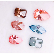 Six fancy color lab grown diamonds displayed on a white background, including pear, marquise, emerald and oval cuts in vibrant pink, blue and cognac tones, precision faceted for fine jewelry settings.