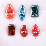 Six fancy color lab grown diamonds displayed on a white background, including pear, marquise, emerald and oval cuts in vibrant pink, blue and cognac tones, precision faceted for fine jewelry settings.