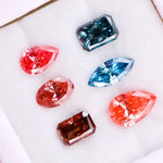 Six fancy color lab grown diamonds displayed on a white background, including pear, marquise, emerald and oval cuts in vibrant pink, blue and cognac tones, precision faceted for fine jewelry settings.