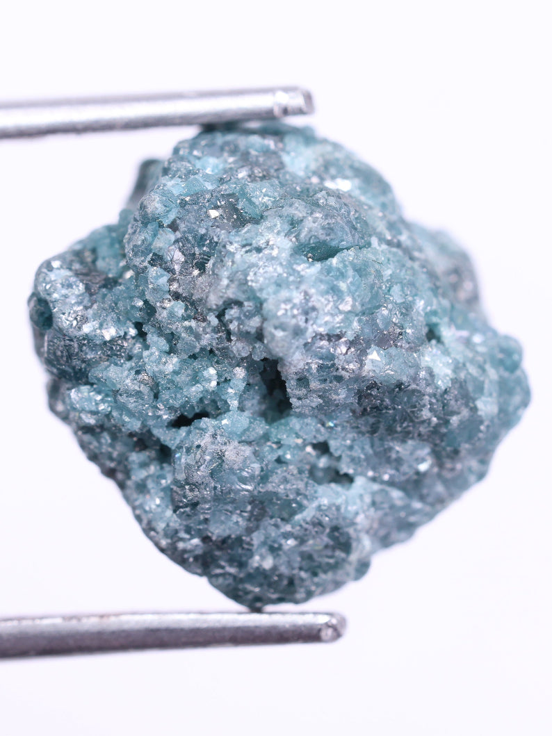 Raw blue diamond held by tweezers on a white background