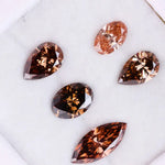 Five lab grown brown and champagne diamonds in pear, oval, and marquise cuts displayed on a white background, showcasing rich cognac tones and brilliant faceting for fine jewelry design.