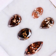 Five lab grown brown and champagne diamonds in pear, oval, and marquise cuts displayed on a white background, showcasing rich cognac tones and brilliant faceting for fine jewelry design.