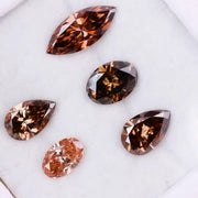 Five lab grown brown and champagne diamonds in pear, oval, and marquise cuts displayed on a white background, showcasing rich cognac tones and brilliant faceting for fine jewelry design.