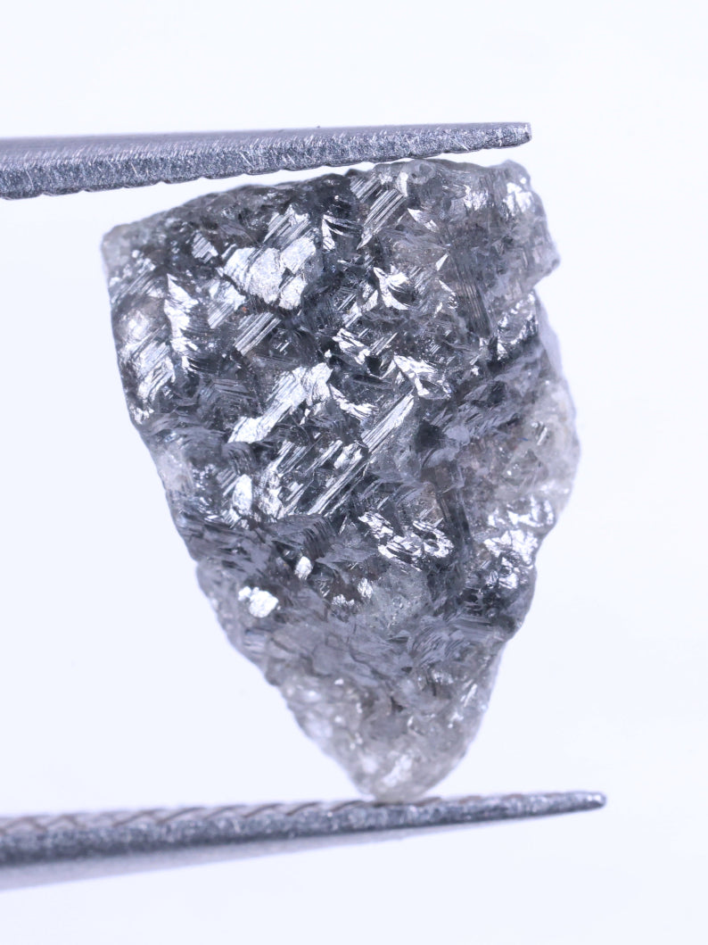 Raw diamond held between tweezers on a white background