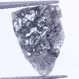 Raw diamond held between tweezers on a white background