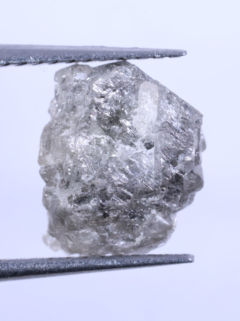 Raw diamond held between tweezers on a light gray background