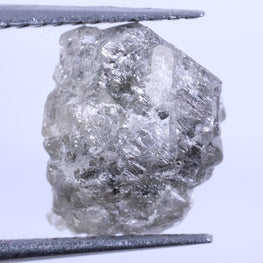 Raw diamond held between tweezers on a light gray background