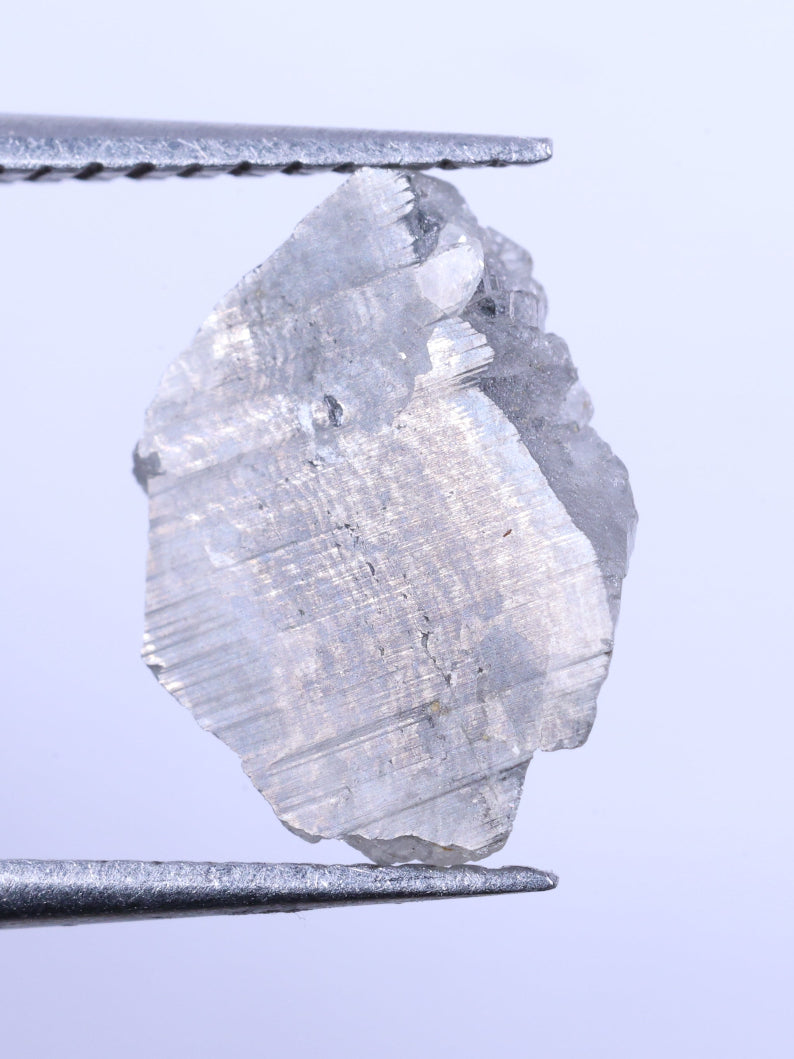 Raw diamond held between tweezers against a light blue background