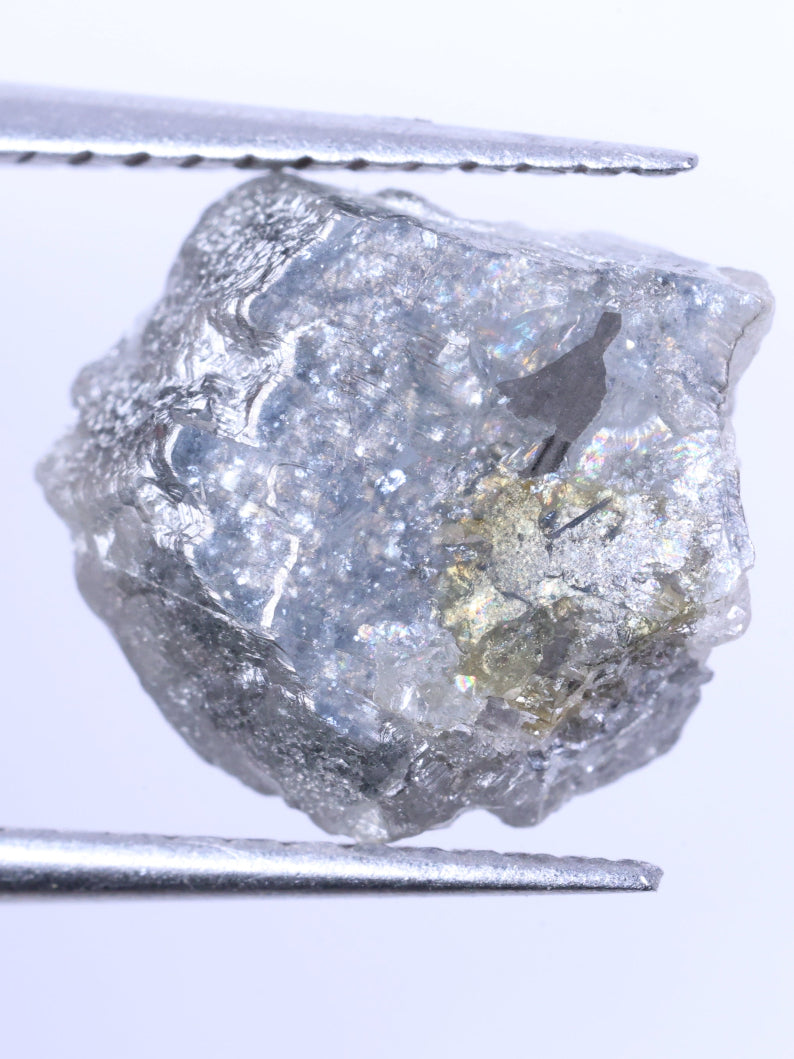 Raw diamond held between tweezers on a white background