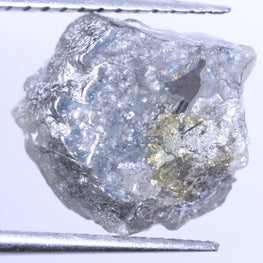 Raw diamond held between tweezers on a white background