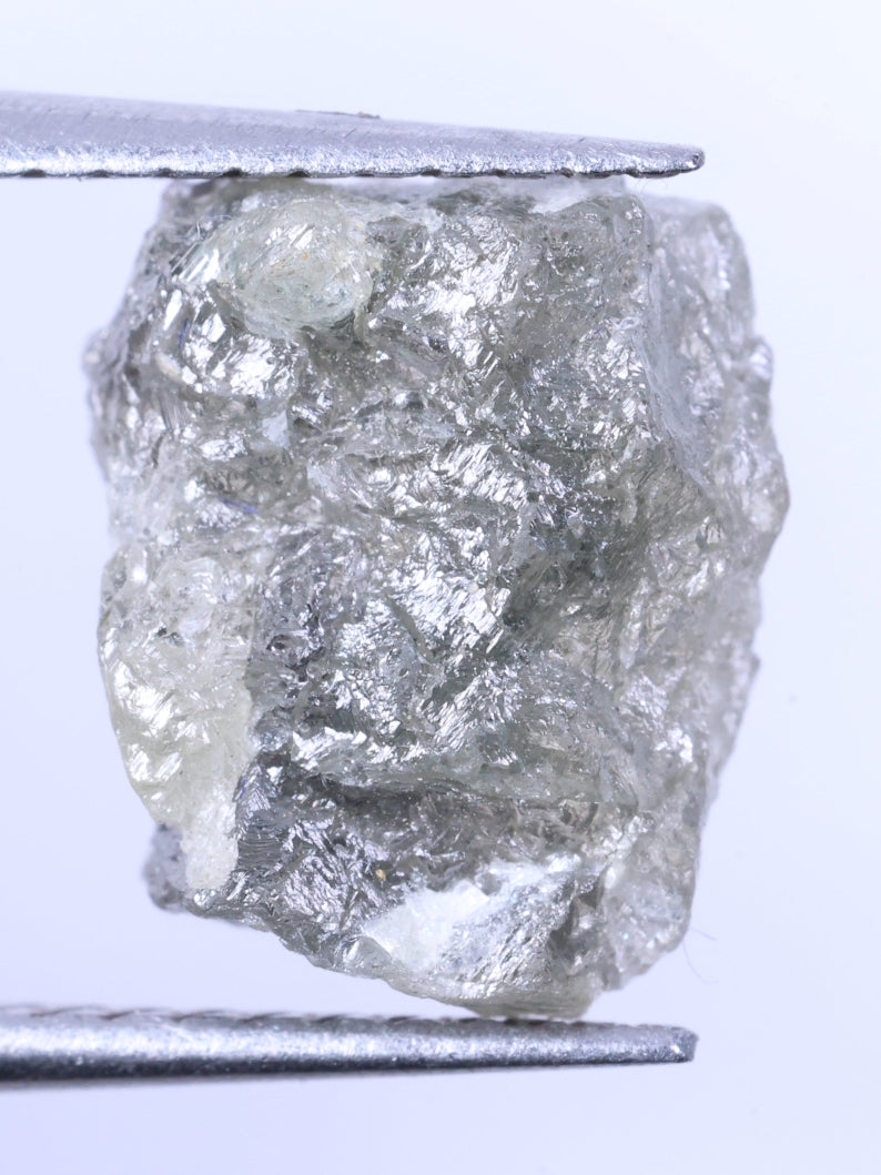 Raw diamond held between tweezers against a light purple background